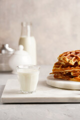 Sweet breakfast - fresh homemade belgian waffles with honey and powdered sugar stacked on white round marble board and small glass with milk