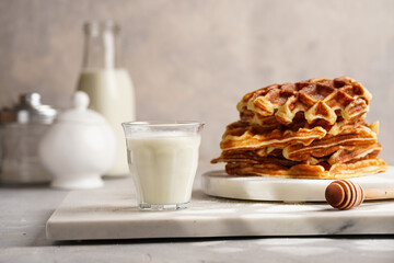 Sweet breakfast - fresh homemade belgian waffles with honey and powdered sugar stacked on white round marble board and small glass with milk