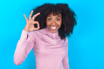 young woman with afro hairstyle in technical sports shirt against blue background hold hand arm...