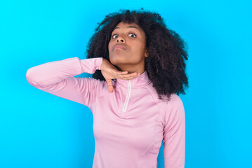young woman with afro hairstyle in technical sports shirt against blue background cutting throat...