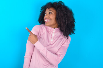 young woman with afro hairstyle in technical sports shirt against blue background glad cheery...