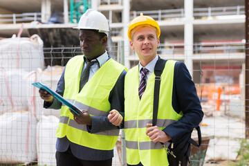 Portrait of two engineers with a folder of working documents standing on the territory of the construction site