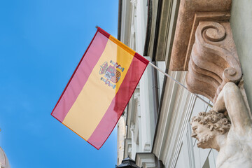 Flag of Spain on the facade of a vintage building against the blue sky