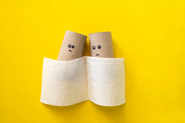 Empty toilet paper roll with sad face for running out of paper on yellow background