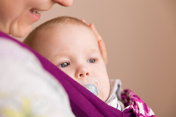 Close-up portrait of a small child with a pacifier in a carrier in the arms of his mother