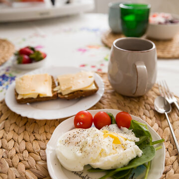 Fried organic eggs on a lettuce leaf. Eggs with tomatoes on a white plate. Sandwiches and a cup of coffee in the background. Healthy breakfast or snack. Healthy food.