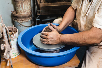Hands of a potter working clay on a potter's wheel. The clay takes the shape the potter gives it with the terracotta tone of the clay.