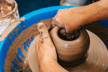 Hands of a potter working clay on a potter's wheel. The clay takes the shape the potter gives it with the terracotta tone of the clay.