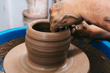 Hands of a potter working clay on a potter's wheel. The clay takes the shape the potter gives it with the terracotta tone of the clay.