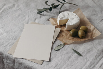 Tasty breakfast, snack still life. Blank greeting card, restaurant menu mockup. Fresh creamy camembert cheese with olive tree fruit, leaves. Grey linen table cloth background. Mediterranean food.