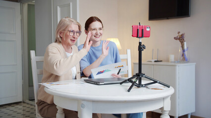 Grandmother and her adult daughter tell their business plan using chart sheets. They film themselves on the phone