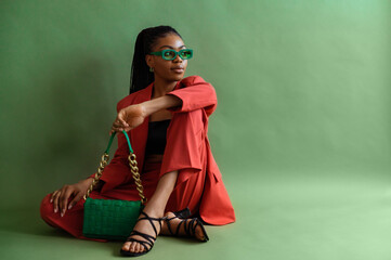 Fashionable elegant Black woman wearing trendy green sunglasses, orange suit with blazer, trousers, strap sandals, leather bag. Full-length studio portrait with natural day light. Copy space for text - 496714042