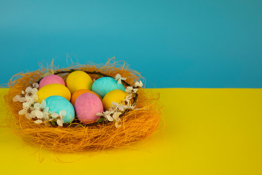 Happy Easter! Easter card with a picture of a nest of colored eggs on a . yellow blue  background decorated with flowers