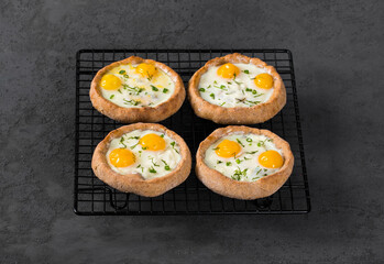 Mini open rye cottage cheese pies with mozzarella, quail eggs and dill, on a serving stand. Dark gray background. 