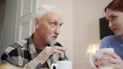 Woman drinking tea and talking to her elderly father