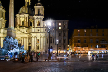Fototapeta na wymiar Night view of Piazza Navona with illuminated cafes, the Sant'Agnese in Agone Church and Fountain of the Four Rivers in Rome, Italy. 