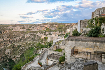 Fototapeta na wymiar Terraces and staircases overlook the street that circles the ancient city of Matera with the Gravina Ravine Canyon below and the sassi caves across in Matera, Italy.