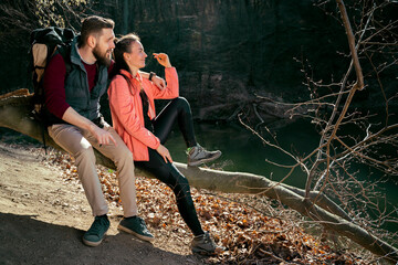 Young couple, man and woman sitting on the tree enjoying time in nature, taking a break from hiking 