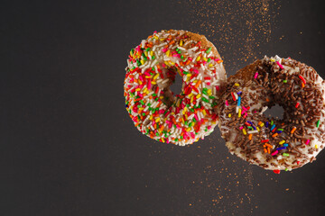Two sweet donuts decorated with multi-colored confectionery sprinkles on a gray background. Sweet food, breakfast for two, birthday, romantic date. There is free space to insert.