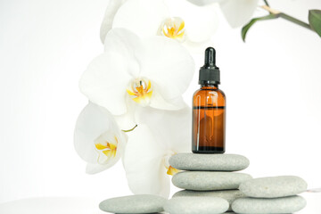 Massage oil and massage stones.Brown glass bottle with massage oil on gray stones and white orchid flower on white background.Spa and aromatherapy.Beauty and relaxation.