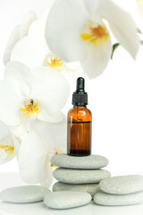 Massage oil and massage stones.Brown glass bottle with massage oil on gray stones and white orchid flower on white background.Spa and aromatherapy.Beauty and relaxation.