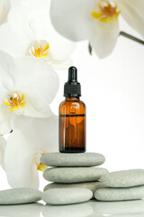 Massage oil and massage stones.Brown glass bottle with massage oil on gray stones and white orchid flower on white background.Spa and aromatherapy.
