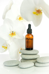 Obraz na płótnie Canvas Massage oil and massage stones.Brown glass bottle with massage oil on gray stones and white orchid flower on white background.Spa and aromatherapy.Beauty and relaxation.