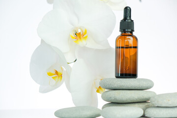 Obraz na płótnie Canvas Massage oil and massage stones. glass bottle with massage oil on gray stones and white orchid flower on white background.Spa and aromatherapy.Beauty and relaxation.