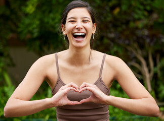 Yoga is about gaining closeness to good vibes. Portrait of a young woman making a heart shape with...