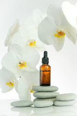 Massage oil and stones.Brown glass bottle with massage oil on gray stones and white orchid flower on white background.Spa and aromatherapy.Beauty and relaxation.