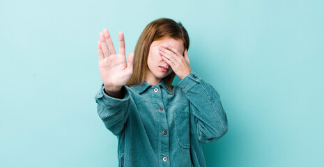 red head pretty woman covering face with hand and putting other hand up front to stop camera,...