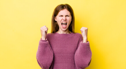 red head pretty woman shouting aggressively with an angry expression or with fists clenched...