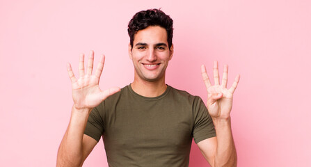 handsome hispanic man smiling and looking friendly, showing number nine or ninth with hand forward,...
