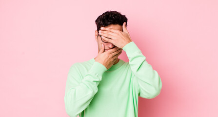 handsome hispanic man covering face with both hands saying no to the camera! refusing pictures or...