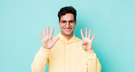 handsome hispanic man smiling and looking friendly, showing number nine or ninth with hand forward,...
