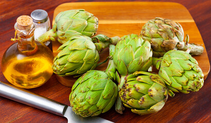 Obraz premium Raw ripe green artichokes, salt and olive oil on wooden table, ingredients for cooking at home