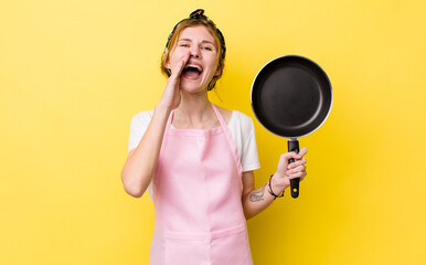 red head pretty woman feeling happy,giving a big shout out with hands next to mouth. fry pan and housewife concept