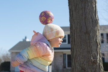 22 month old toddler playing with a ball outside on a warm winter day; ball grazes top of her head...
