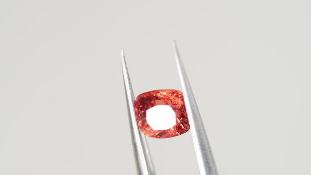 Orange spinel gem in tweezers. Jewelry shopping for birthday, Valentine Day, other holiday. Gemologist or jeweller holding burmese spinel, macro shot on gray background