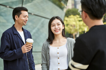 three young asian adults man woman standing talking outdoors on street