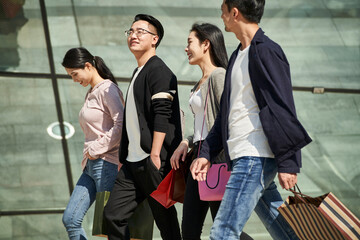 group of young asian people talking chatting conversing while walking on street with shopping bags