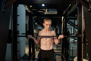 Fototapeta na wymiar Shirtless young athlete doing reverse grip barbell lift in gym to build triceps muscles
