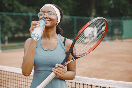Black american female tennis player drinking water on the court outdoors