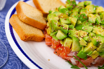 Closeup of appetizing fresh raw salmon tartare with diced avocado sprinkled with sesame seeds...