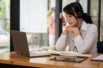 Asian female students wear headphones to learn languages online. watch and listen to the teacher Video call webinars e-learning at home concepts distance education girl looking at laptop screen