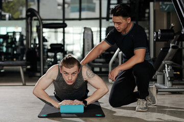 Fit young man doing push-up exercise under control of his fitness trainer in gym