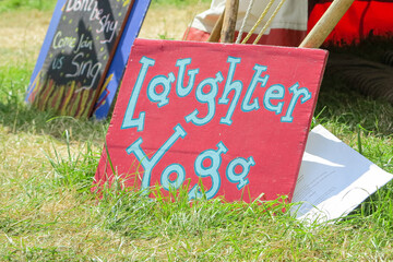 Glastonbury, England - A sign advertising Laughter and Yoga leaning against a tent in The Healing Fields at Glastonbury Festival 2019.