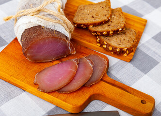 Thinly sliced cured pork sirloin meat with spices served with rye bread on wooden cutting board