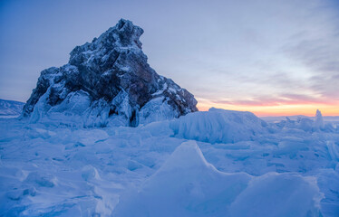 A rock surrounded with cracked ice and ice hummocks during sunrise on beautiful winter frozen Baikal lake