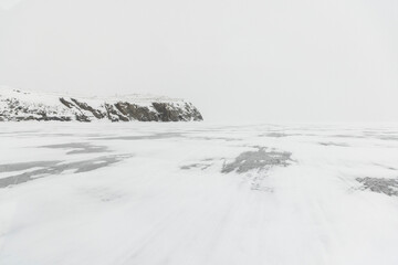Baikal lake in the fog, snow-covered ice and cliffs in the background